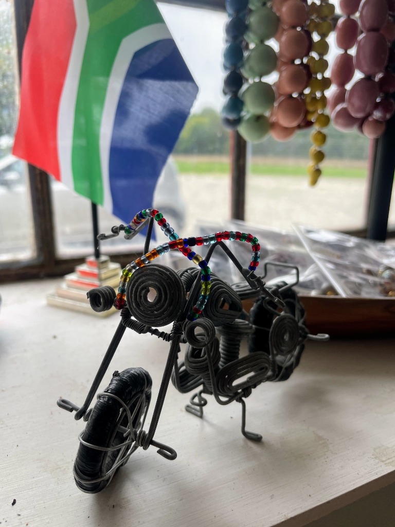 Håndlavet trådmotorcykel fra sydafrikansk wire art-tradition med det sydafrikanske flag og farvestrålende perlesmykker i baggrunden