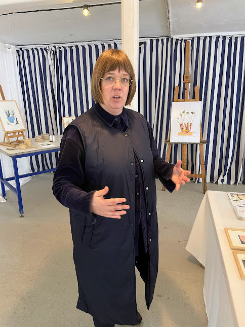 Trine Schjermer gestikulerer og fortæller engageret foran staffelier med kunst