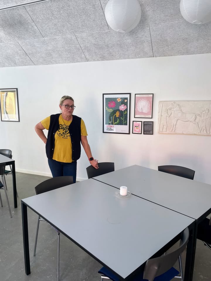 Værtinden i det lyse selskabslokale med langborde og kunst
