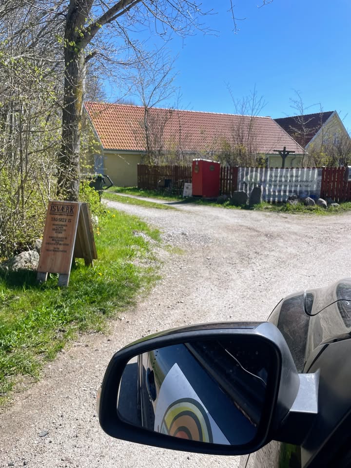 Kig fra bilens sidespejl mod indkørslen og skiltet for Isværk Tag-selv is